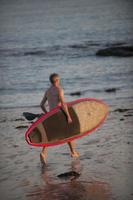 hombre con su tabla de paddle en la playa al atardecer