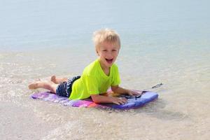 Niño montando en boogie board en el océano foto