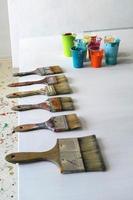Different Size Wide Paintbrushes In A Row With Paint Cups photo