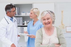Paciente sonriendo mientras el médico y la enfermera discutiendo en segundo plano.