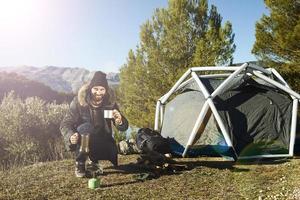 Man camping drinking coffee near tent smiling happy outdoors in