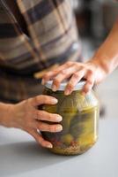 closeup on young housewife opening jar of pickled cucumbers photo
