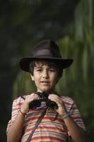 Niño con sombrero de aventurero mirando con binoculares. foto