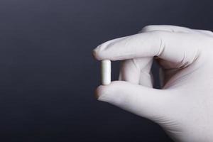 Hand in white latex glove holding a capsule photo