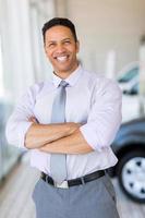 vehicle salesman with arms crossed in car showroom photo