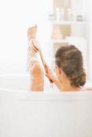 mujer joven en la bañera con cepillo corporal en la pierna foto