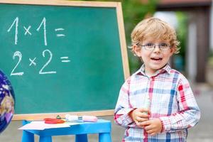 Cute little kid boy with glasses at blackboard practicing mathem photo