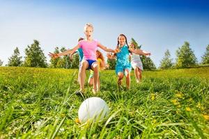 Grupo de niños corriendo hacia la pelota en la pradera foto