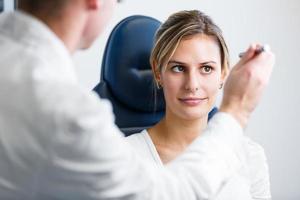 Pretty young woman having her eyes examined by optometrics photo