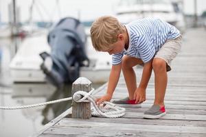 Young boy ties knot on boat dock