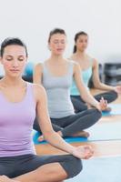 Women in lotus posture with eyes closed at fitness studio