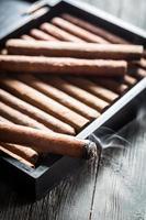 Smoke rising from a burning cigar on wooden humidor photo