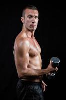 Portrait of confident shirtless athlete working out with dumbbell