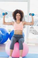 Mujer haciendo ejercicio con pesas en la bola de la aptitud en el gimnasio
