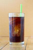 Cola con hielo y paja en vidrio sobre fondo de madera foto