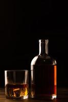 Vaso de whisky con hielo y botella en mesa de madera. foto