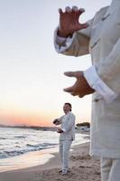 Two older people practicing Taijiquan on the beach at sunset