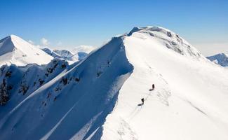 Two trekkers on a sharp, snowy mountain ridge.