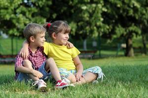 boy and little girl sitting on grass in park photo