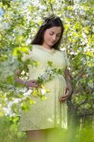 soñadora hermosa mujer embarazada caminando en el floreciente jardín de primavera foto