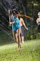 Girl with friends playing in lawn sprinkler