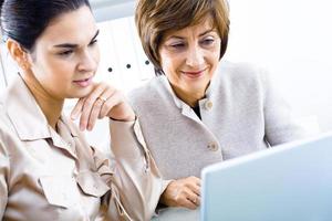 Two businesswoman looking at blue laptop while at work