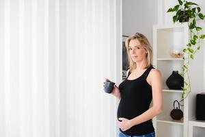 alegre mujer embarazada madura de pie en casa bebiendo té foto