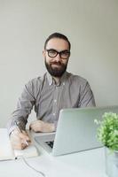 Hombre con barba en gafas tomando notas con bloc de notas portátil