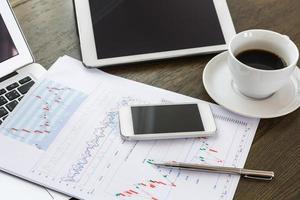 computadora portátil, tableta, teléfono inteligente y taza de café con documentos financieros