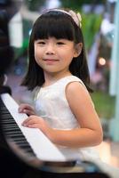 Little girl wearing white dress playing piano photo