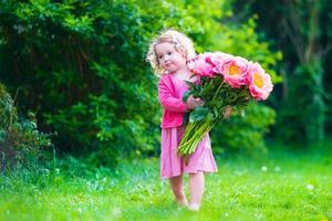 Adorable little girl with peony flowers in the garden