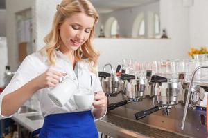 Pretty female barista pouring some milk in cup photo