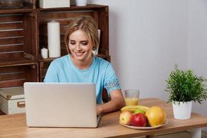 Young blonde woman looking for a recipe information on laptop photo
