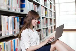 Hermosa estudiante asiática estudiando en la biblioteca con laptop