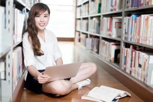 Hermosa estudiante asiática estudiando en la biblioteca con laptop