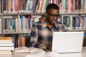 feliz estudiante masculino africano con laptop en biblioteca foto