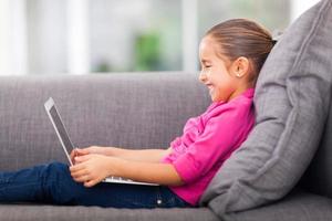 little girl using laptop on sofa photo