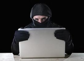 hombre pirata informático en negro con computadora portátil concepto de delito cibernético foto