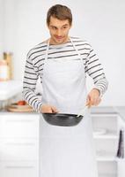 handsome man in apron with frying pan at kitchen photo