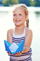 Cute little girl holding origami boat outdoors photo