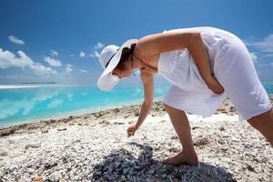 mujer caucásica recogiendo conchas marinas en la playa foto