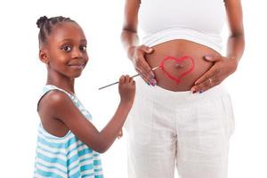 Little african american girl painting on her mother's belly photo