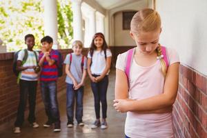 Sad schoolgirl with friends in background at school corridor