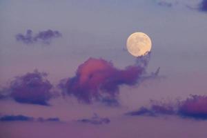 la luna llena se eleva a través de las nubes en un cielo nocturno púrpura