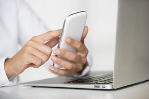 Female hands holding smartphone in front of laptop photo