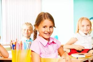 niña de la escuela y otros alumnos sentados en escritorios foto