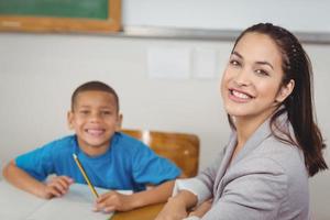 Smiling teacher and her pupil sitting at desk
