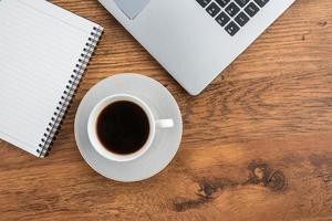 Laptop, notebook y taza de café en la mesa de trabajo foto