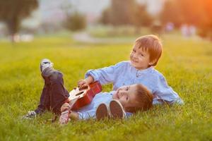 Two adorable boys, sitting on the grass, playing guitar