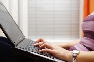 Mujer escribiendo en la computadora portátil, usando la computadora sentado en el piso de su casa foto